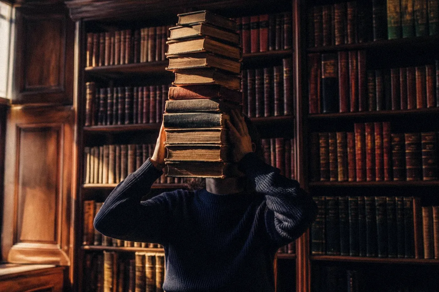 Personne dans une bibliothèque, visage caché derrière une pile de livres